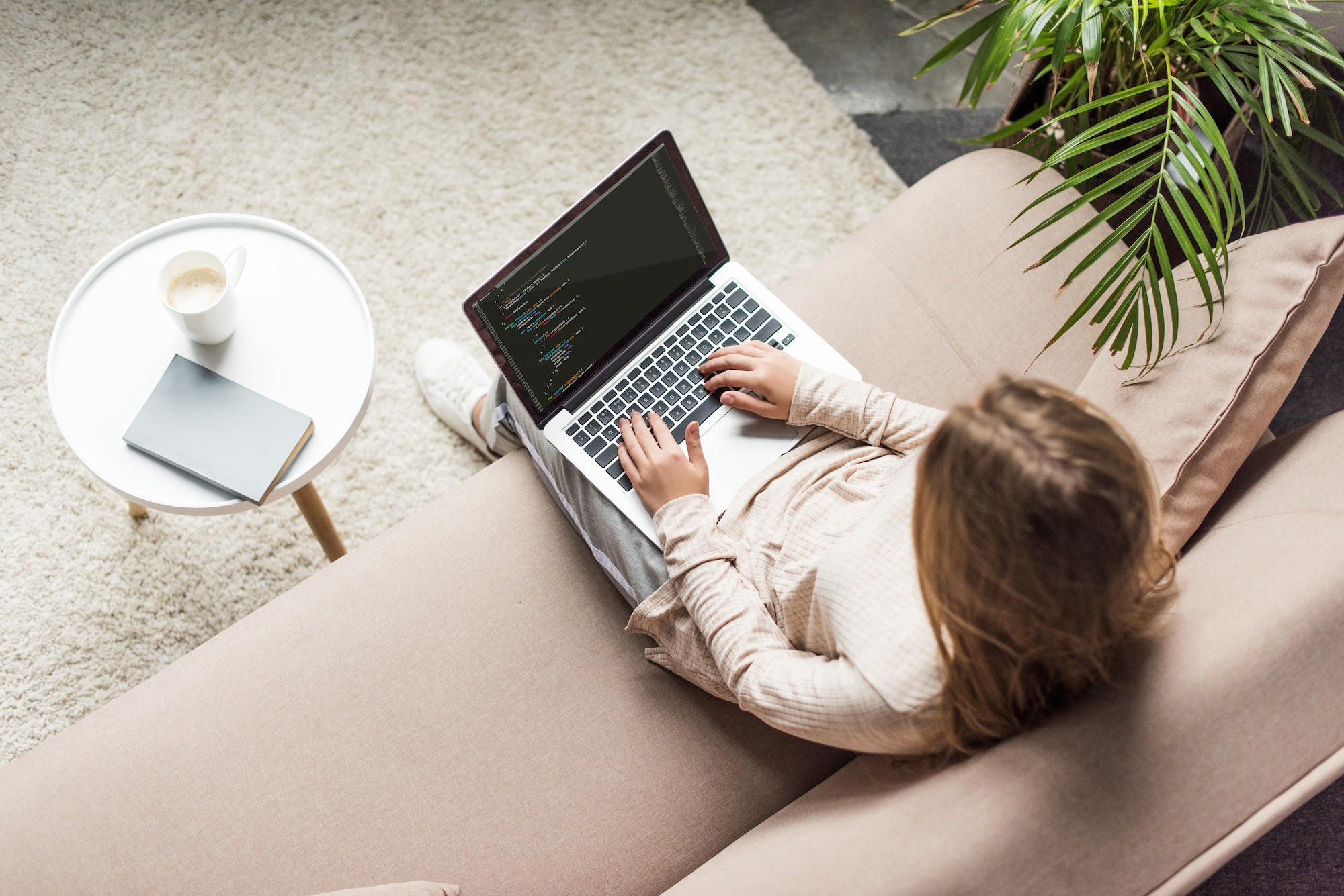 high angle view of young female developer coding with laptop on couch